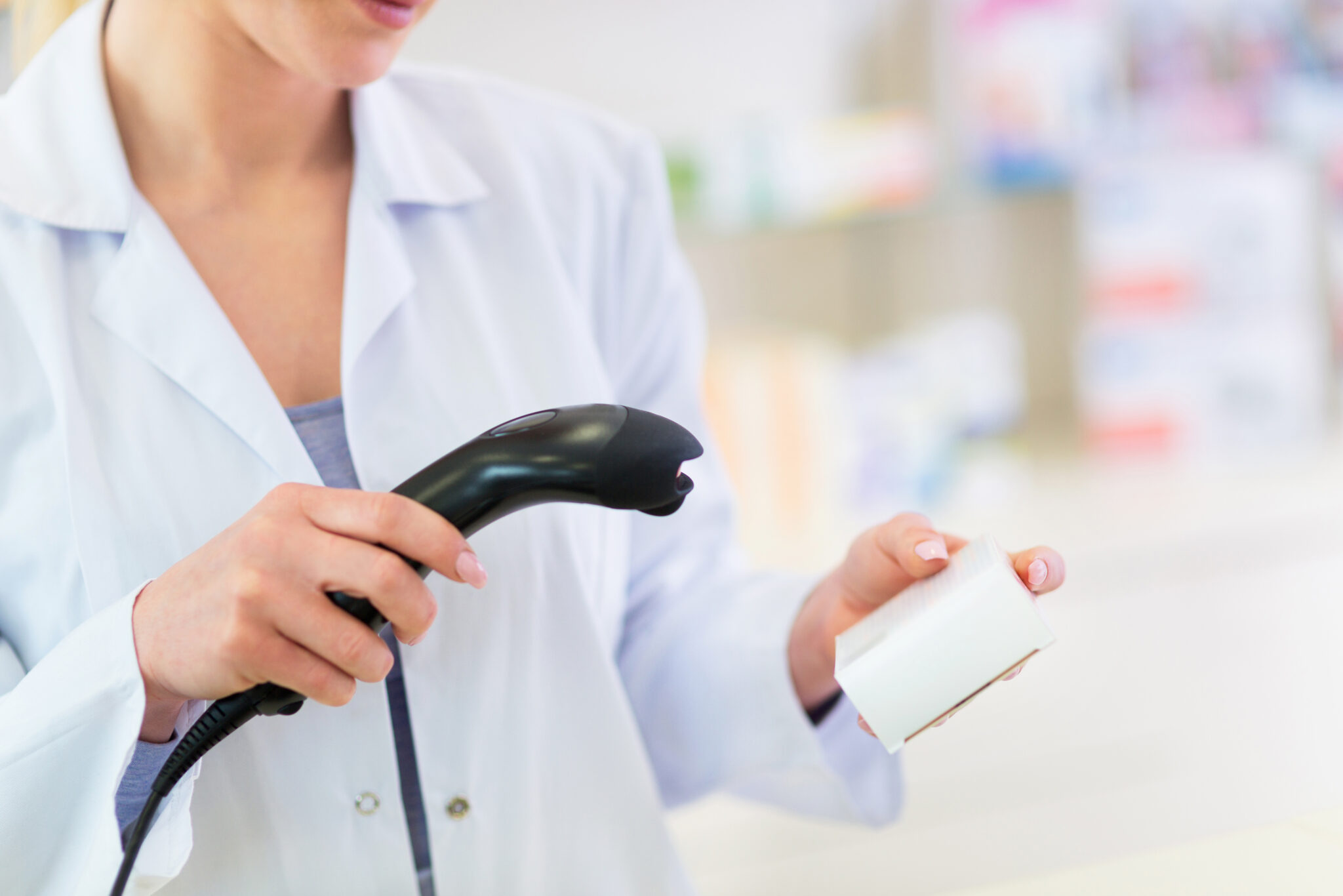 Un farmacéutico con una bata blanca de laboratorio escaneando una caja de medicamentos recetados